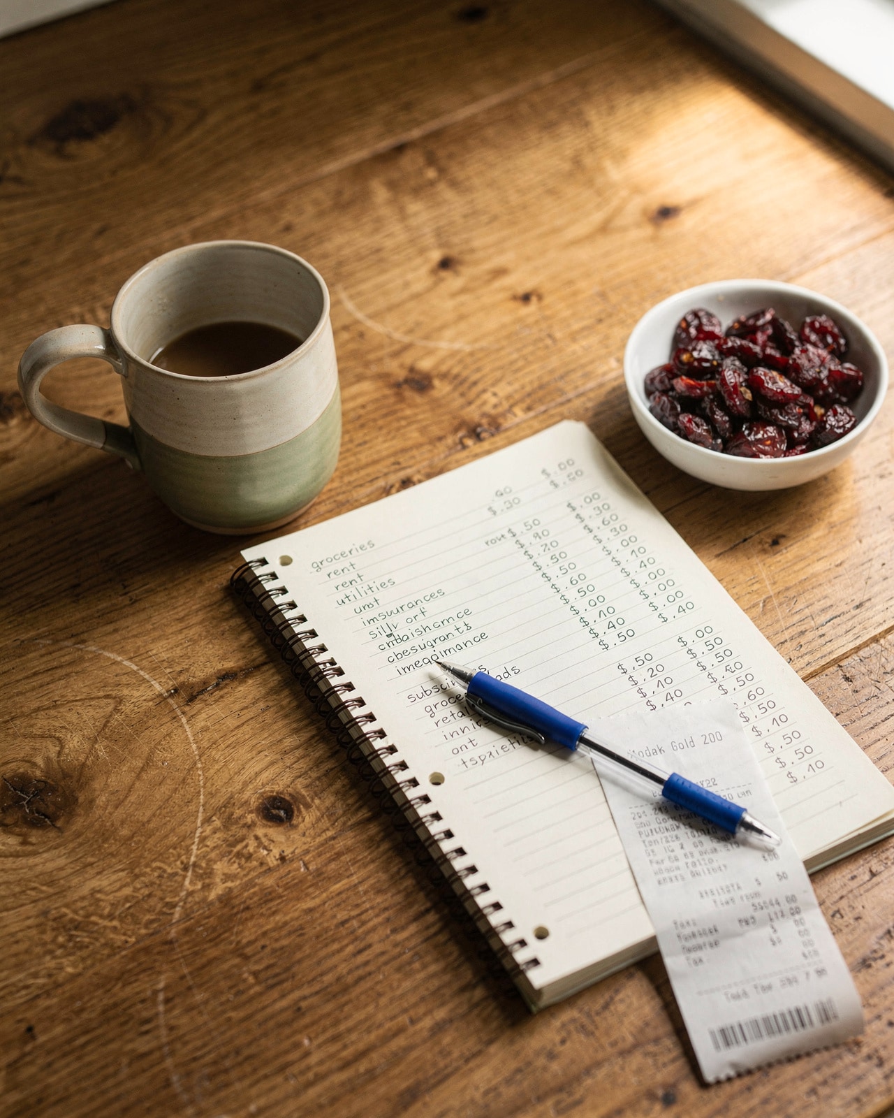 Open notebook with a handwritten household budget, pen, and ceramic mug on a kitchen table in morning light.
