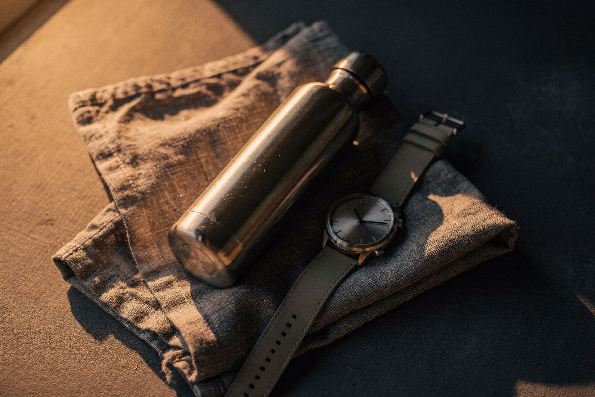 Steel water bottle and smartwatch resting on folded linen in warm window light