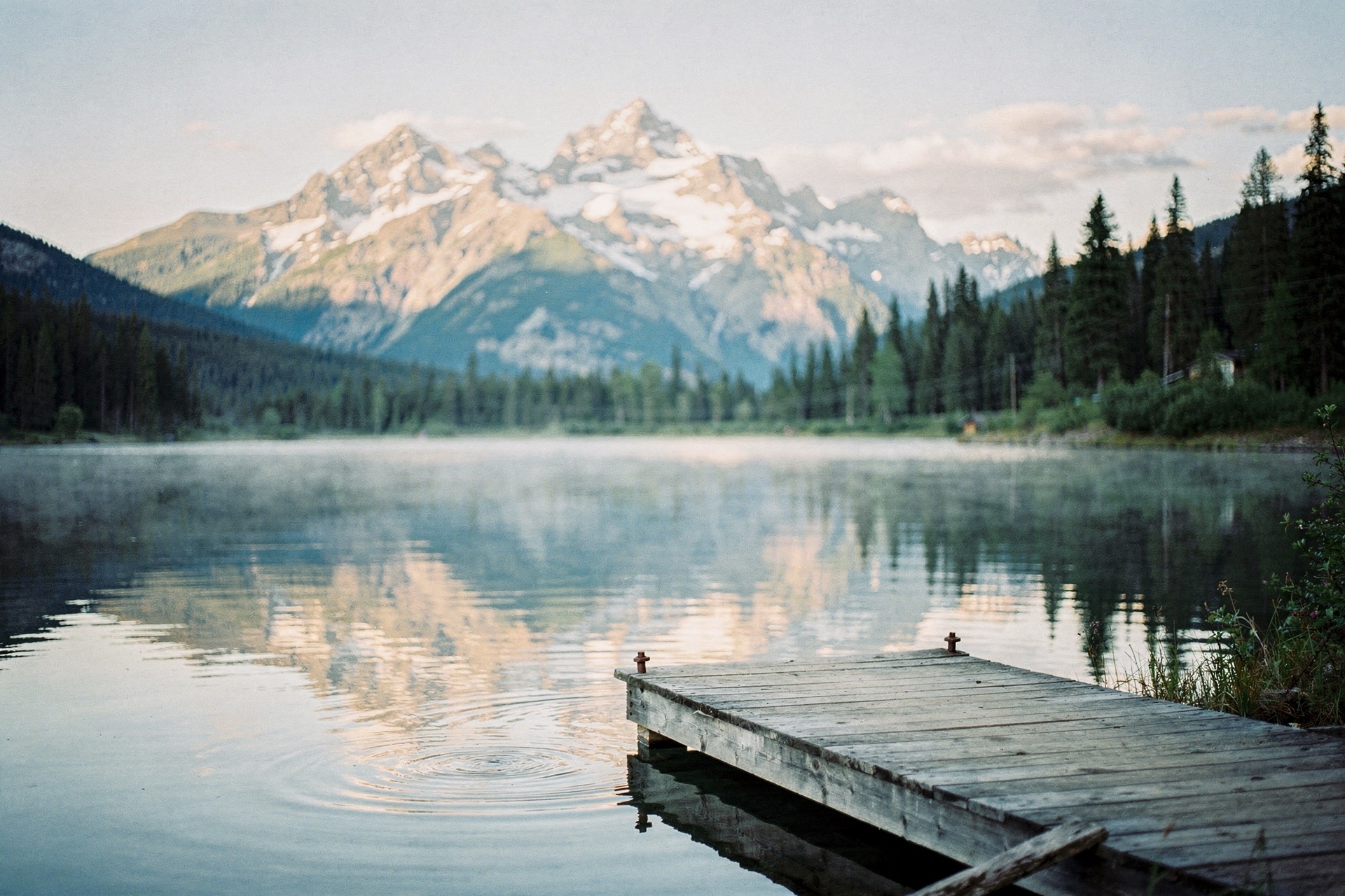Still alpine lake at clear bright morning with snow-capped peaks reflected and a small wooden dock