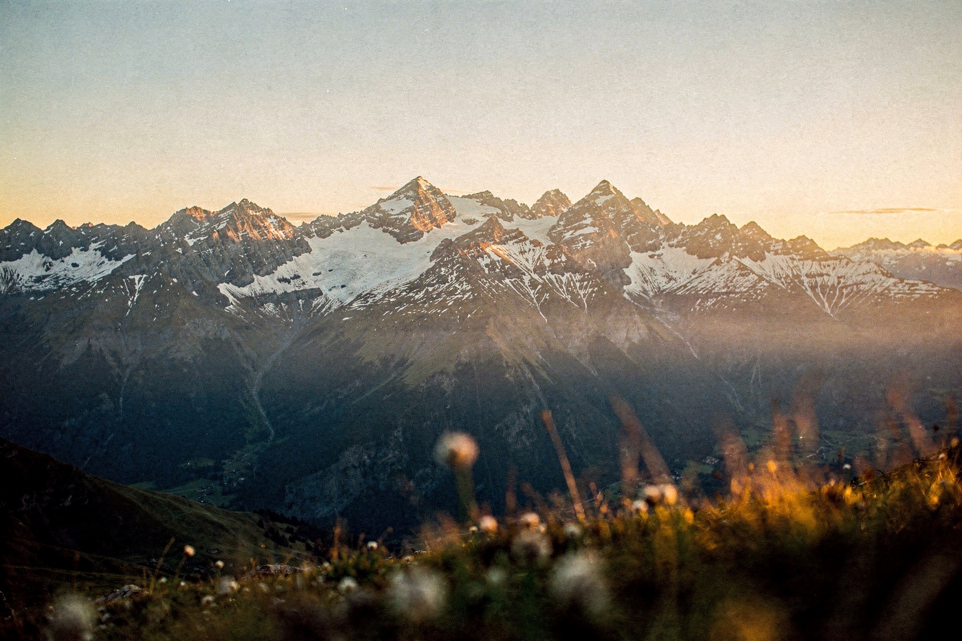 Distant snow-capped mountains at golden sunset with warm amber light raking across the ridgelines