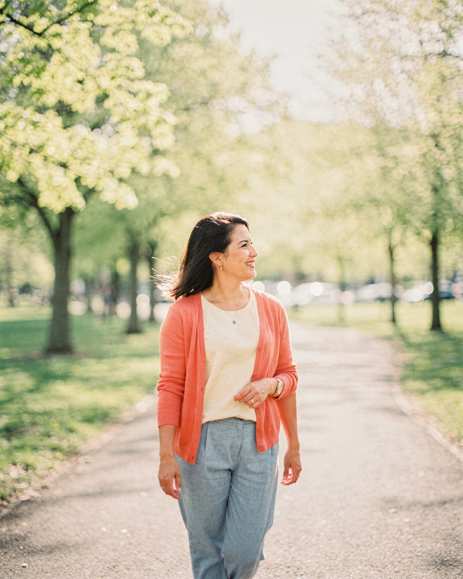 Woman walking calmly on a sunlit park trail in late spring morning, looking off at the trees