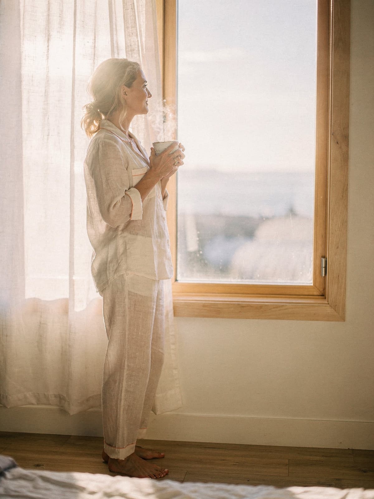 Same woman at a sunlit window holding a coffee mug, soft profile
